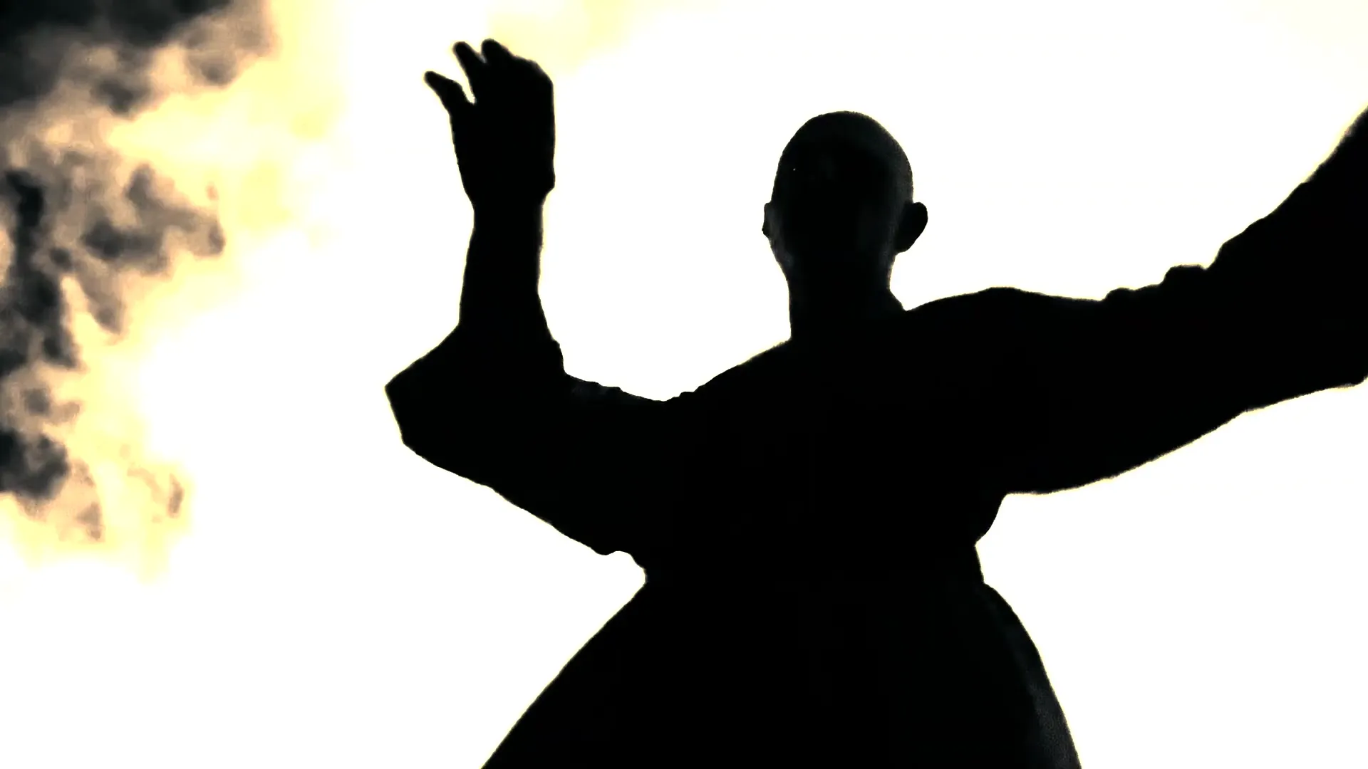Reza Safinia in silhouette, arms raised, against pale flame and drifting smoke
