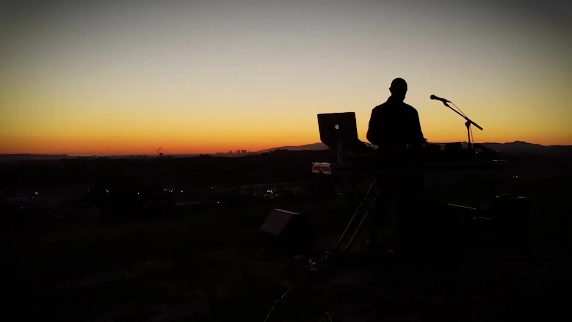 Reza Safinia and his instruments silhouetted on a hilltop against an orange sunset