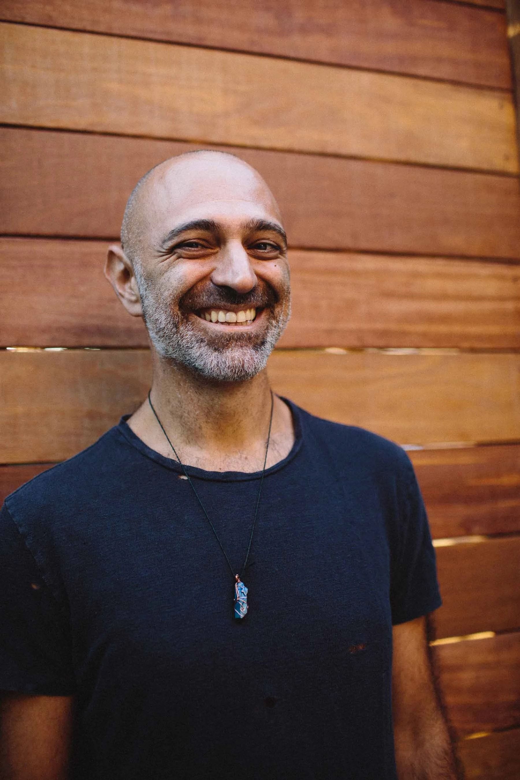 Reza Safinia smiling against a wooden wall
