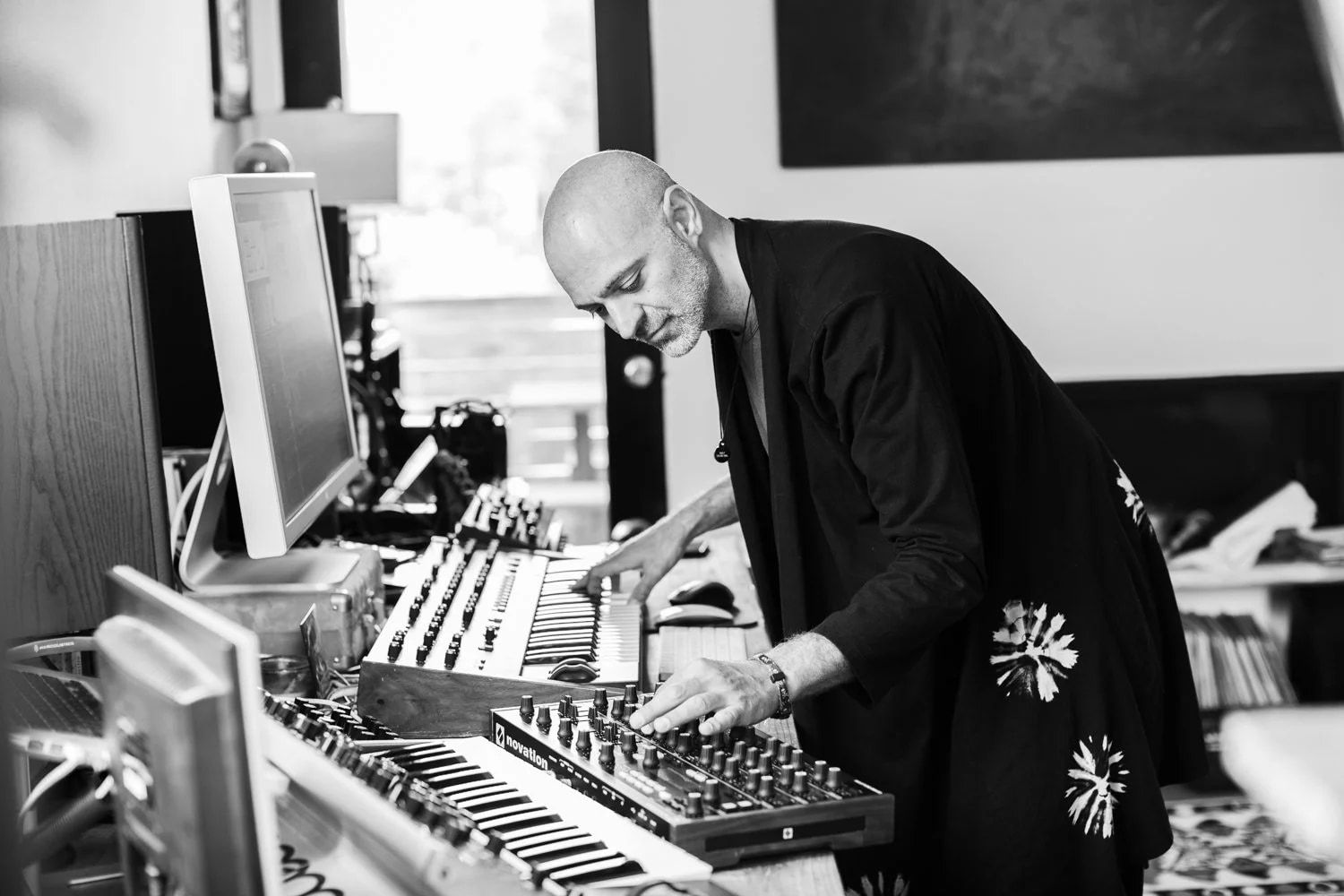Reza Safinia in black and white, working at a bank of synthesisers